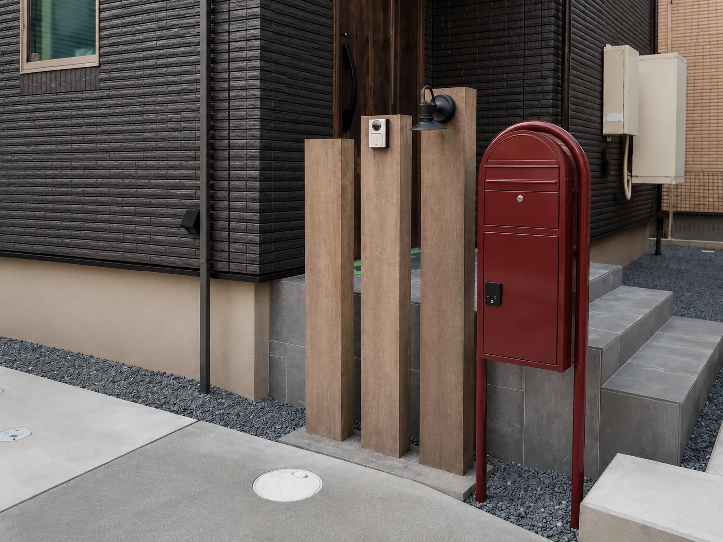 印西市の外構施工事例。ボルドー色のボビカーゴポストと木調スリーパー門柱、玄関まわりのデザイン。